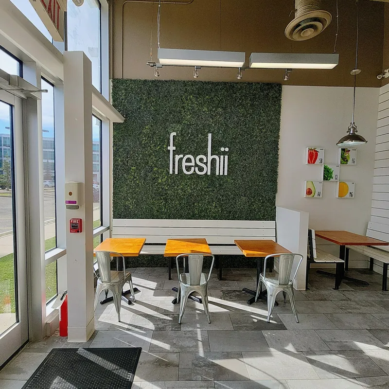 Dine-in tables in front of the Freshii green wall at Freshii Sundance restaurant in Sunpark Plaza, SE Calgary.